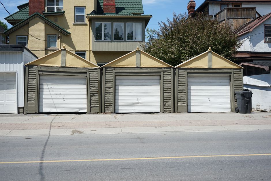 Row of three traditional residential garages with unique roof design on a sunny day.